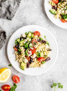 Oil-free and vegan Greek pasta salad on a small white plate with lemon and tomatoes.