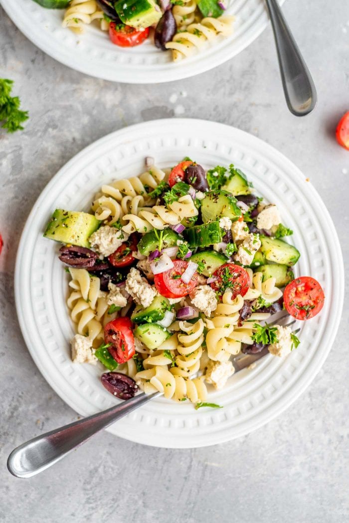 Rotini pasta with cucumber, olives, tomato and tofu feta on a small white plate.
