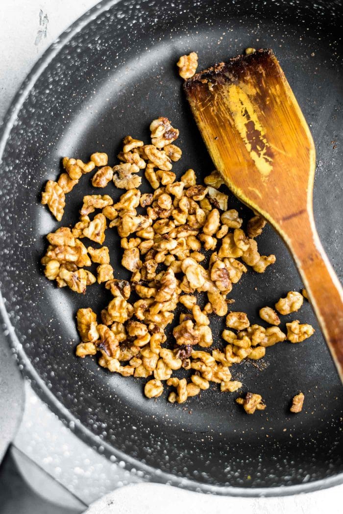 Chopped walnuts in a black skillet with a wooden spoon.