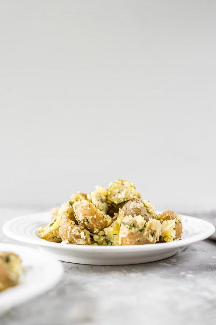 Dijon potato salad with dill on a white plate against a grey background.
