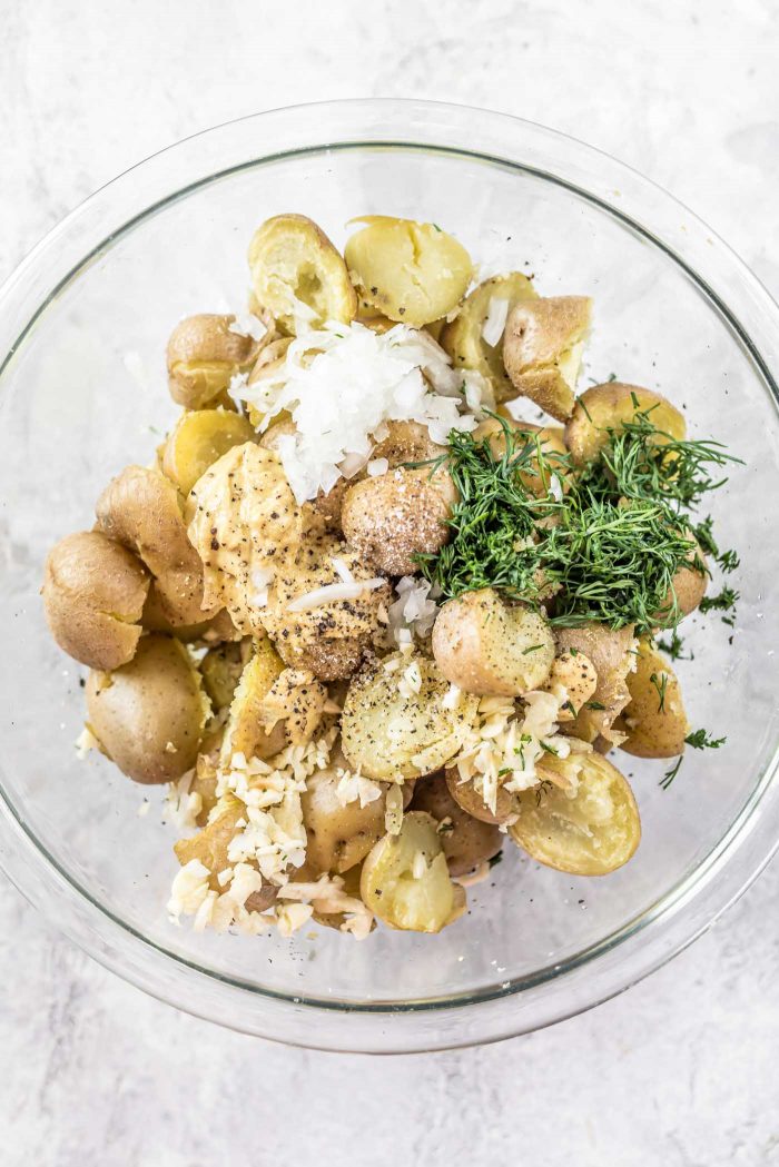 Cooked baby potatoes in a glass bowl with shallot, dill and dijon mustard.