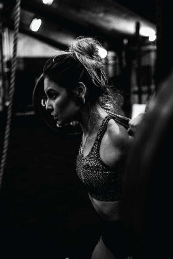 Fit woman looking determined with a barbell on her back.