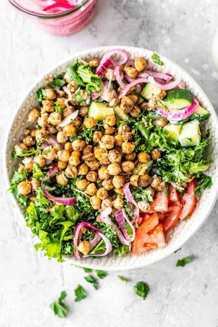 Shawarma-spiced chickpeas in a bowl with kale, tomato, cucumber, parsley and pickled red onion.