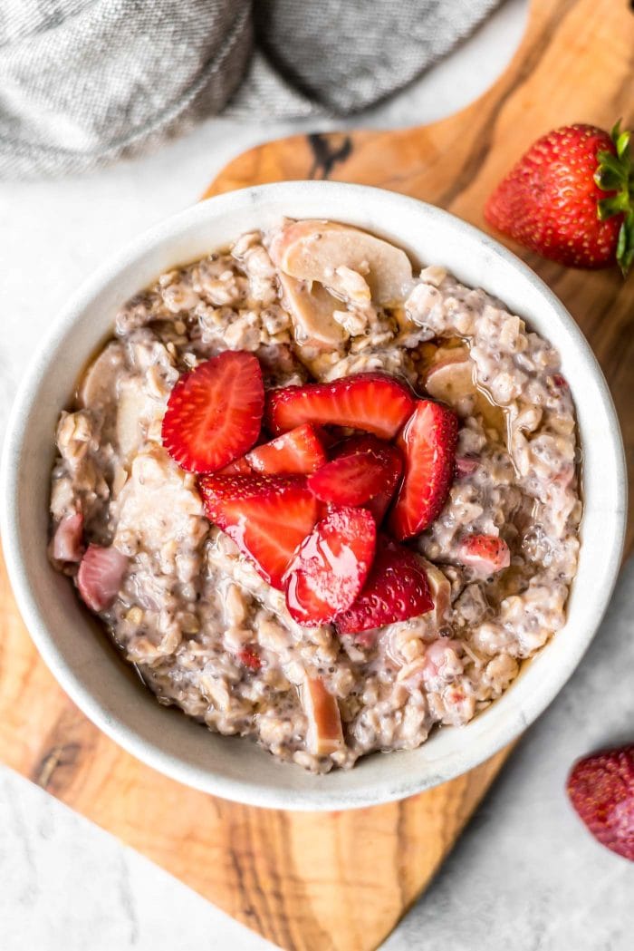 Bowl of rhubarb oatmeal topped with chopped strawberries.