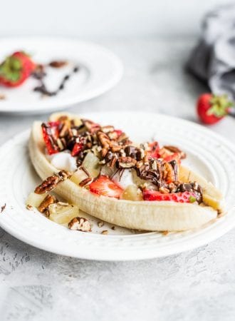A vegan banana split with dairy-free yogurt, pecans and strawberries on a white plate.