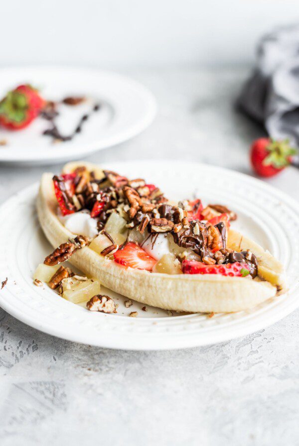 A vegan banana split with dairy-free yogurt, pecans and strawberries on a white plate.