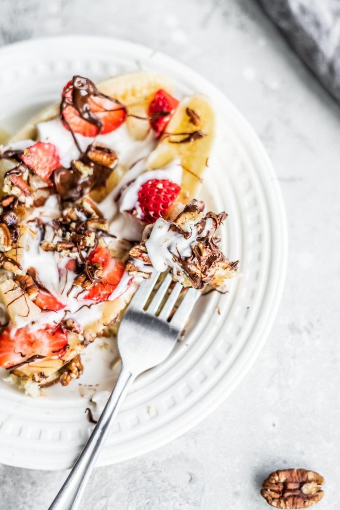 Close up of a banana topped with strawberries, pecans, yogurt and a drizzle of chocolate on a plate.