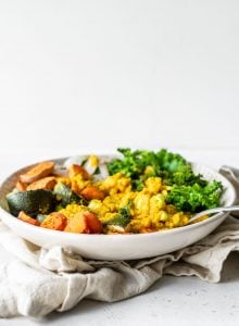 Bowl with lentils, roasted vegetables and kale against a white background.