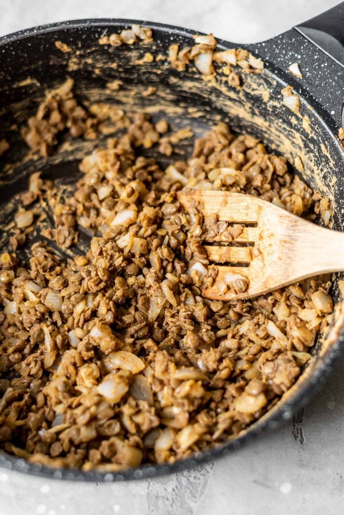 Lentil taco meat with onions in a skillet with a wooden spoon.