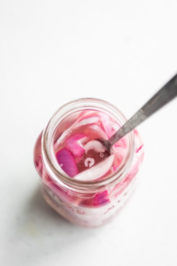 A jar of pickled red onions with a spoon in it.