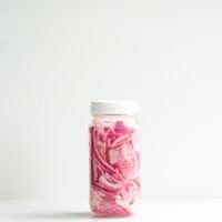 Sealed glass jar of quick pickled red onions against a white background.