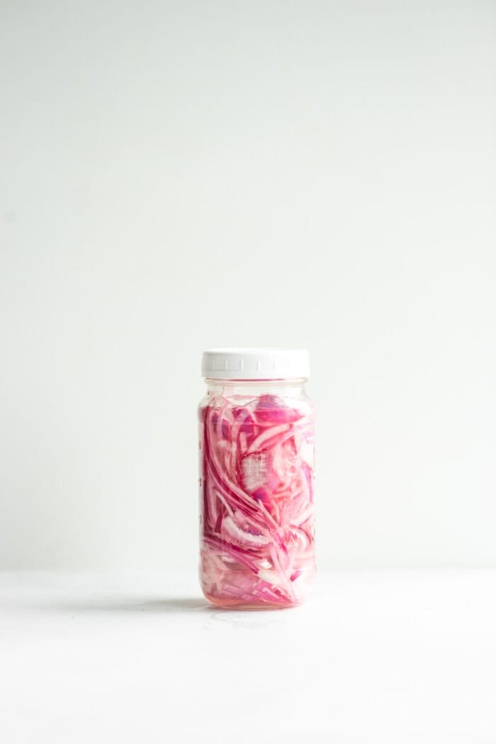 Sealed glass jar of quick pickled red onions against a white background.