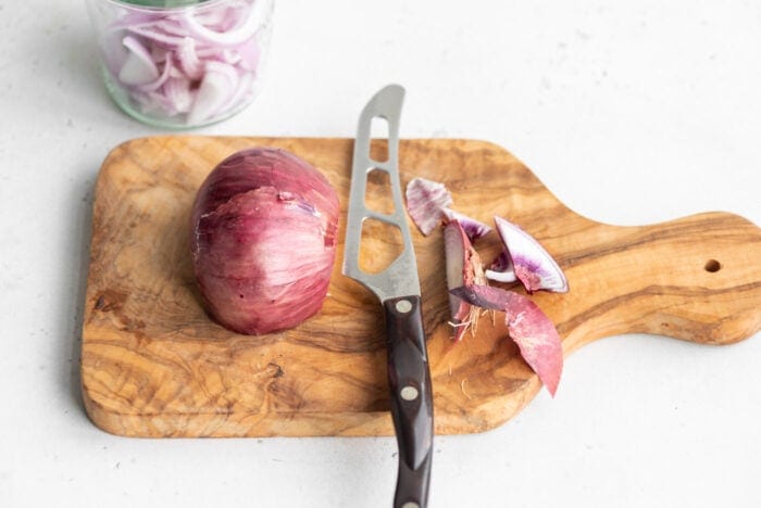Half of a red onion with the ends sliced off on a cutting board.