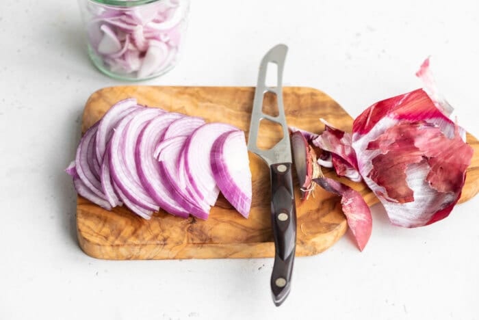 Half of a red onion sliced into thin pieces on a cutting board.