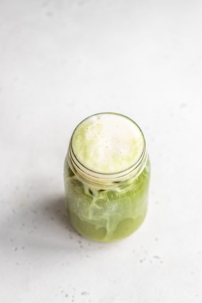 Overhead shot of an iced matcha latte in a glass jar against a grey background.