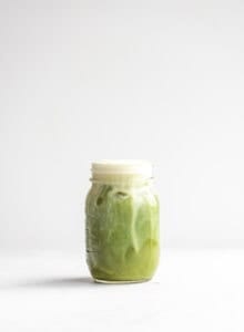Dairy-free almond milk iced matcha latte in a glass jar against a white background.