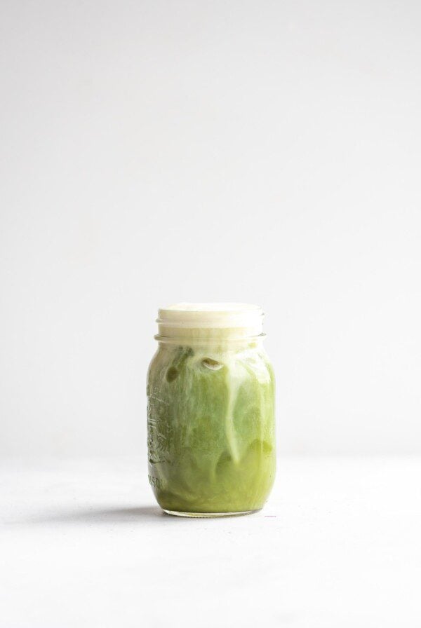 Dairy-free almond milk iced matcha latte in a glass jar against a white background.