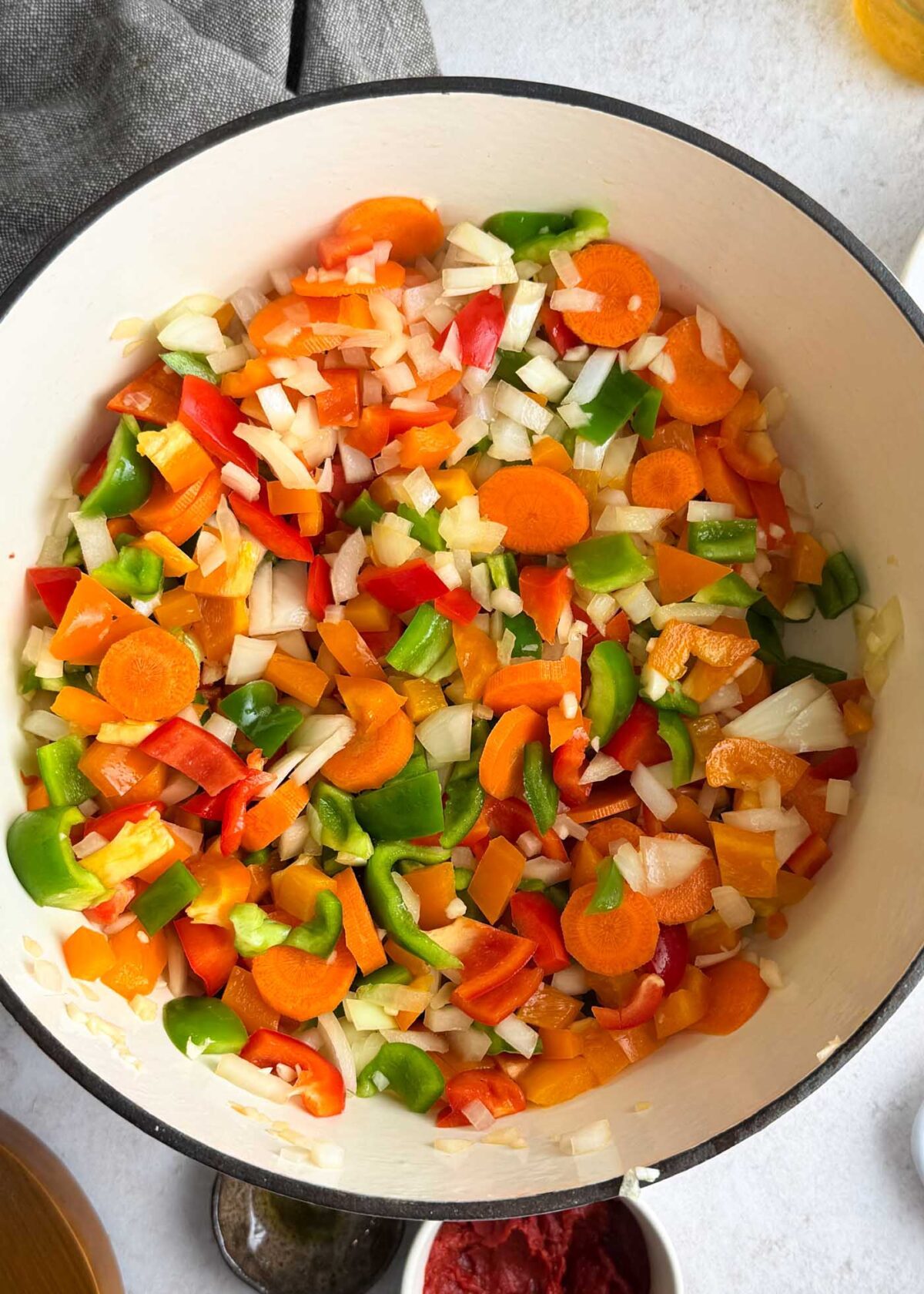 Onions, carrots, bell peppers cooking in a large pot.