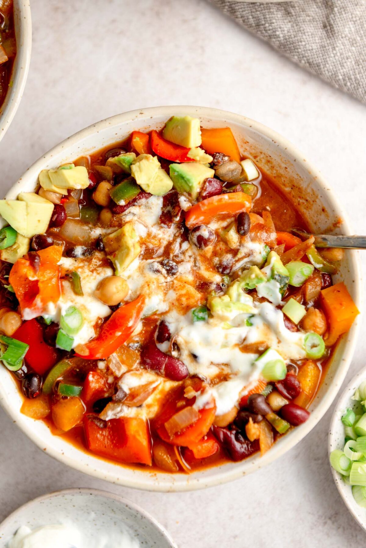 Chili topped with sour cream, avocado and green onion in a bowl.