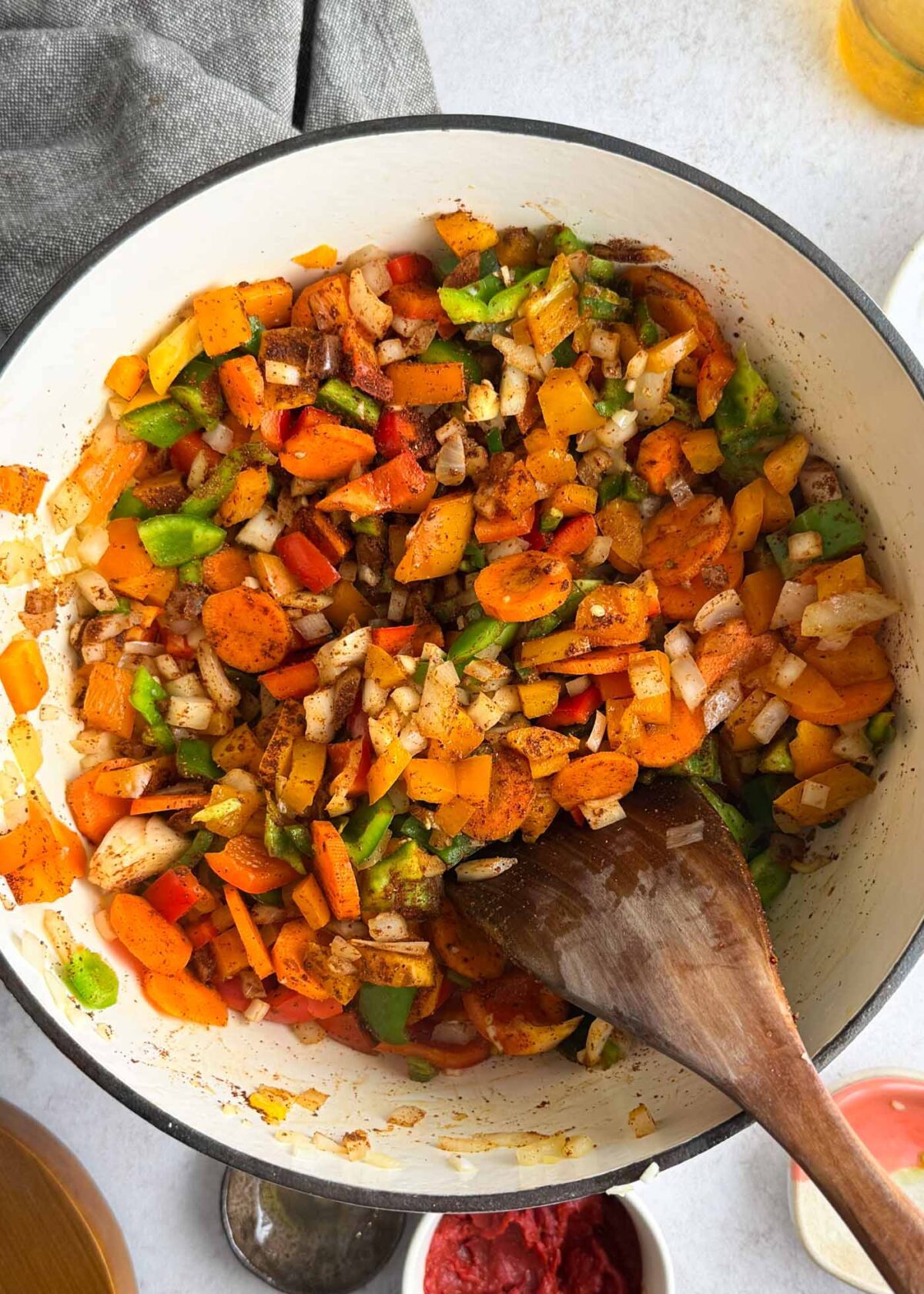 Onions, carrots, bell peppers cooking in spices in a large pot.