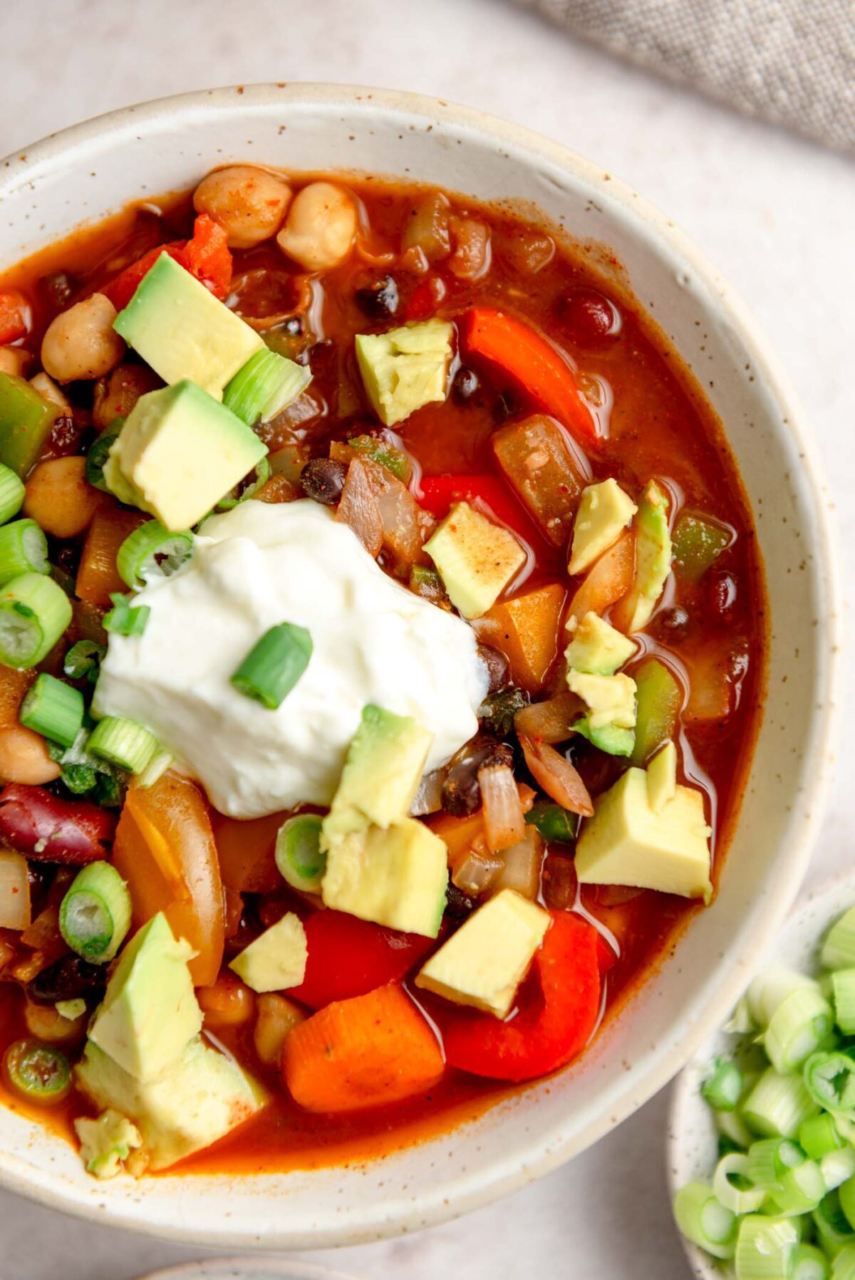 Bowl of three bean chili topped with sour cream, avocado and green onions.