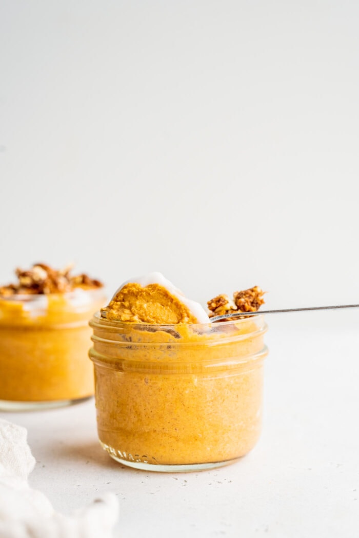 A spoon scooping pumpkin mousse out of a jar.