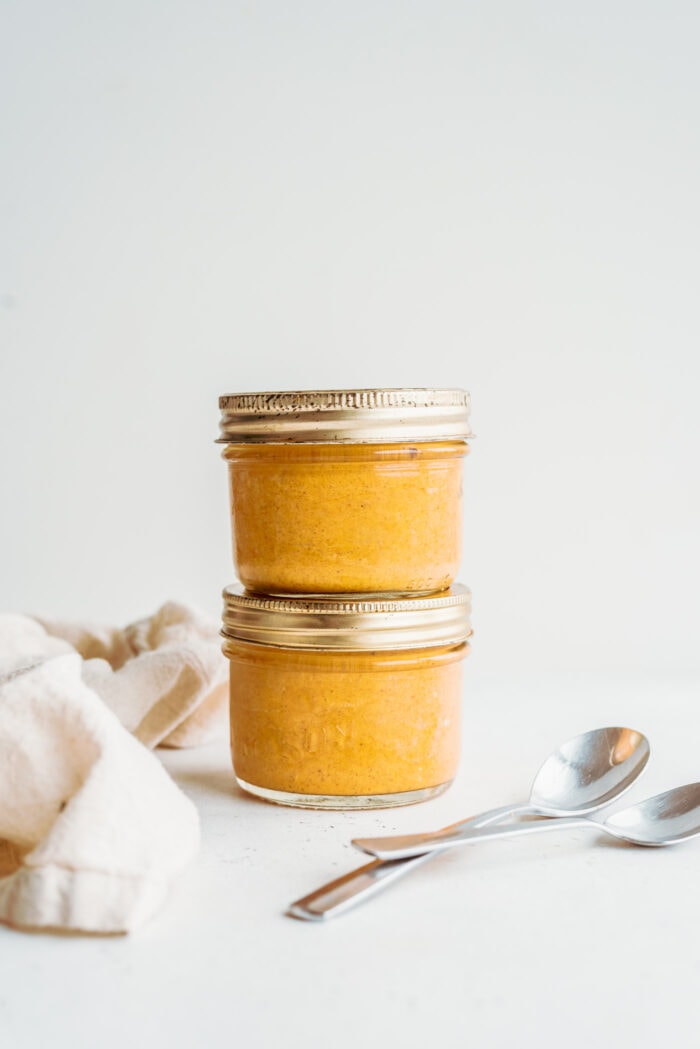 Two stacked mason jars of pumpkin mousse with two spoons beside them.
