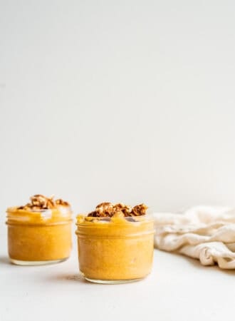 Two jars of pumpkin mousse topped with yogurt, nuts and dates.