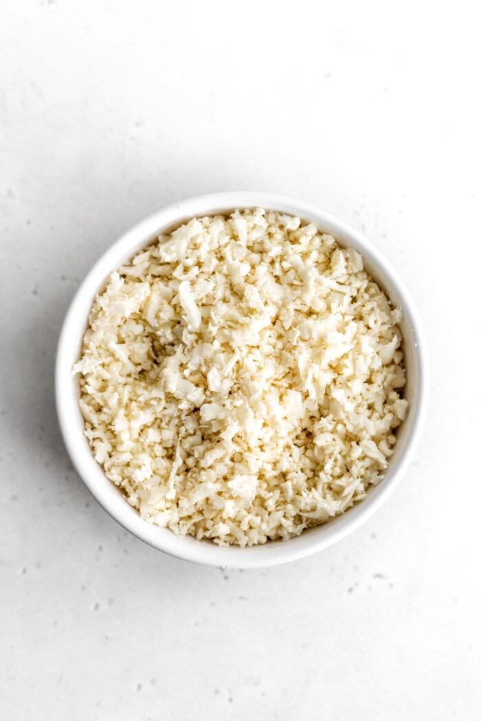 White bowl of cauliflower rice sitting on a white surface.