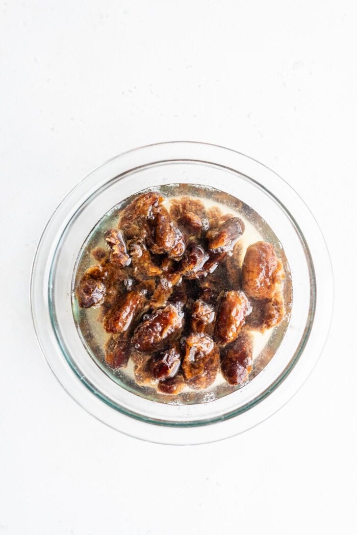 Pitted dates soaking in hot water in a glass bowl.