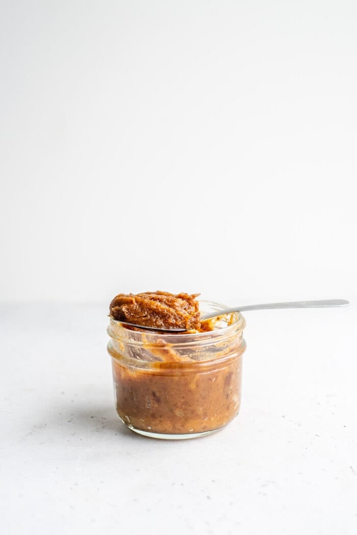 A spoon scooping thick date paste out of a mason jar.