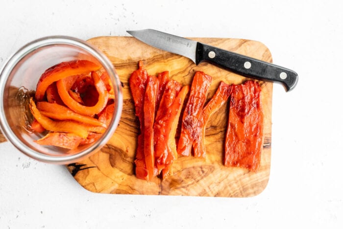 Sliced roasted red peppers on a cutting board.