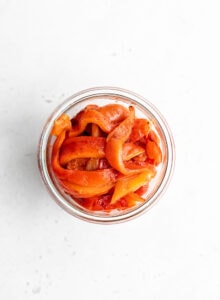 Overhead shot of sliced roasted red peppers in a jar.