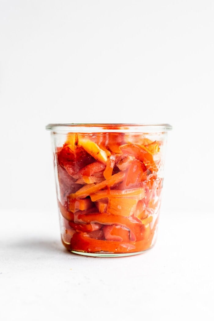 Jar of sliced roasted red peppers against a white background.