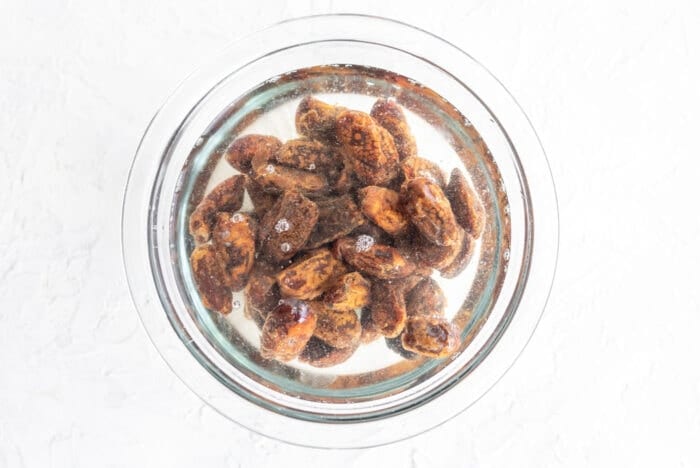Glass bowl filled with dates and water sitting on a white surface.