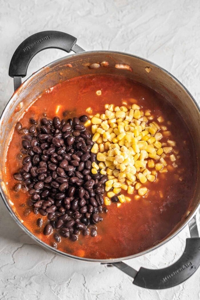 Black beans and corn being stirring into a pot of chili.