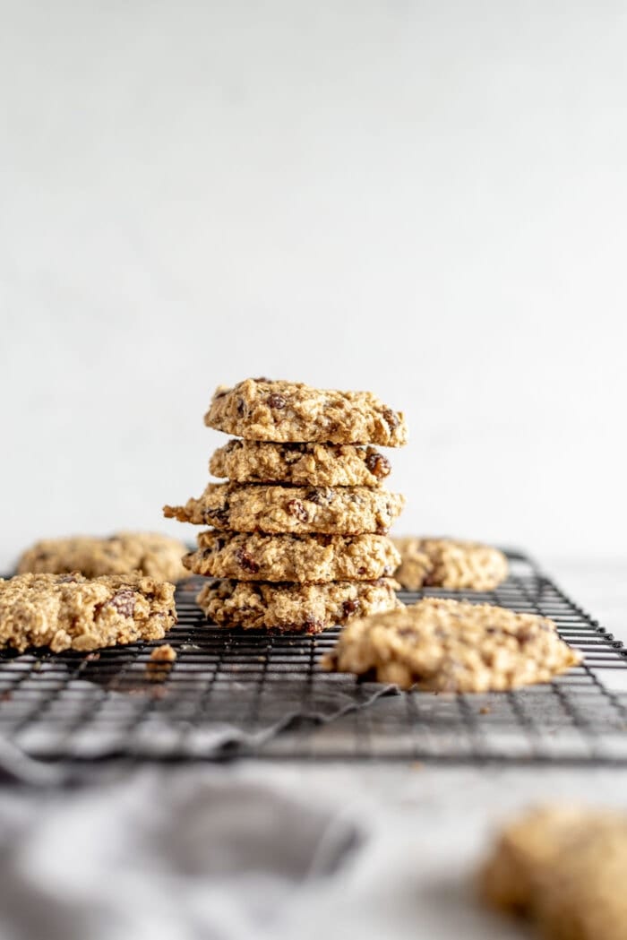 A stack of vegan and gluten-free, healthy oat cookies sitting on brown paper with some raisins scattered around.