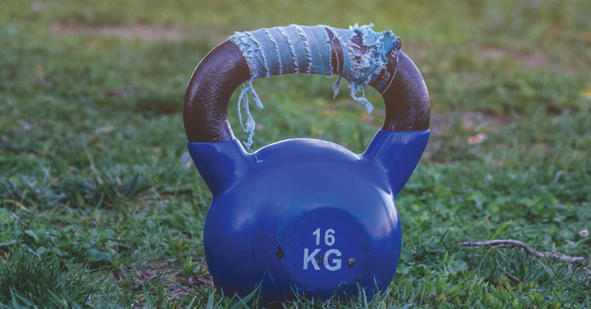 A blue kettlebell sitting in a grassy field.