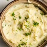 A serving dish full of vegan mashed potatoes topped with fresh parsley.