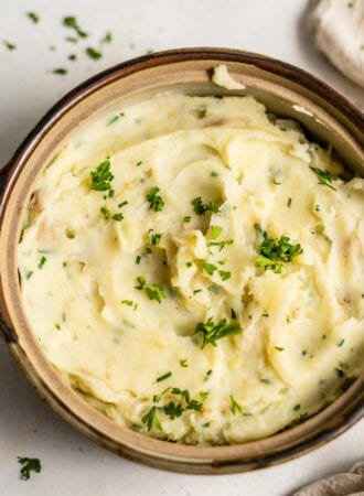 A serving dish full of vegan mashed potatoes topped with fresh parsley.