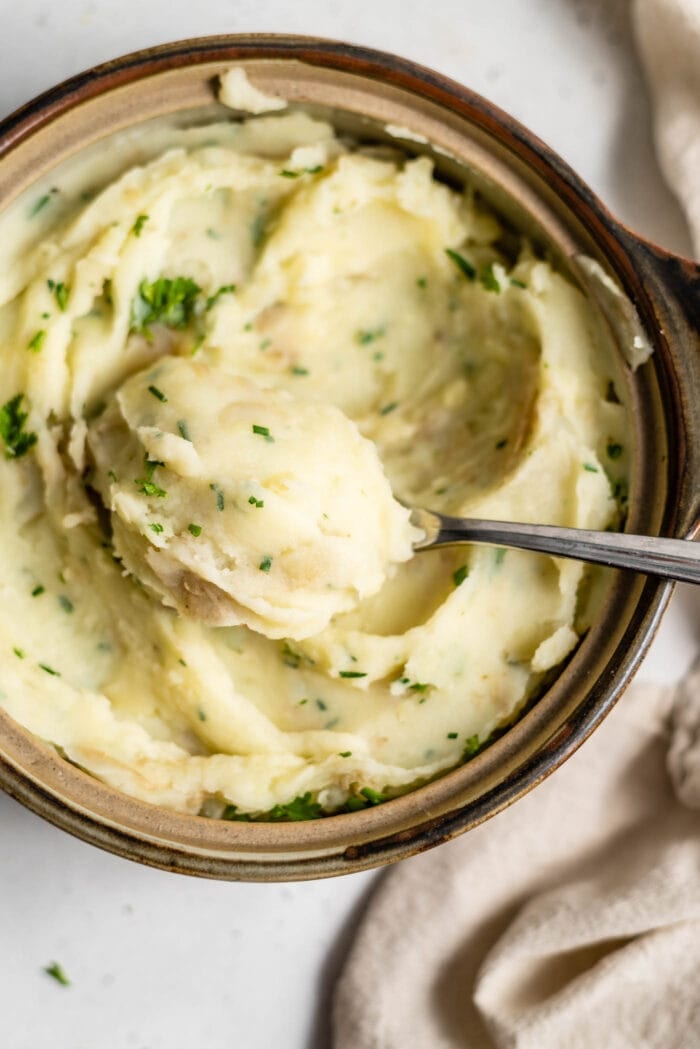 A spoon scooping a large spoonful of mashed potatoes out of a serving dish.