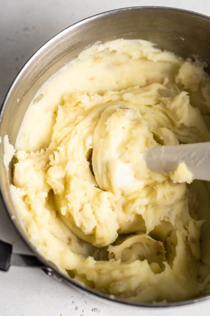 An immersion blender mixing mashed potatoes in a large pot.