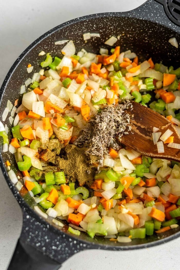 Dried herbs being added to a skillet of sauteed vegetables.