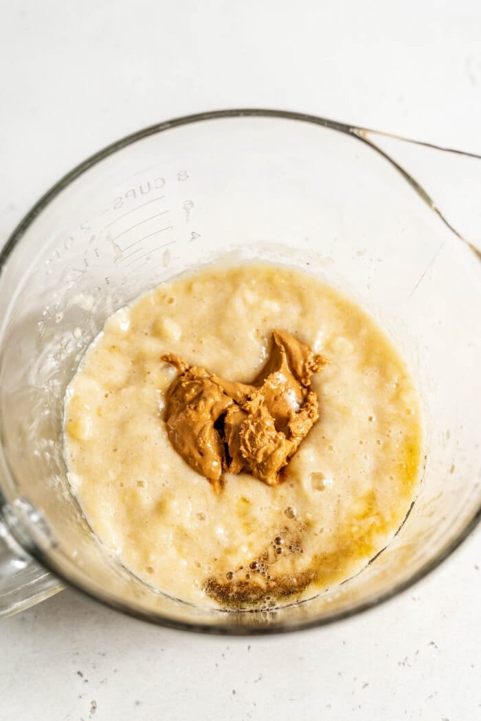 Mashed banana, nut butter and maple syrup in a glass mixing bowl.