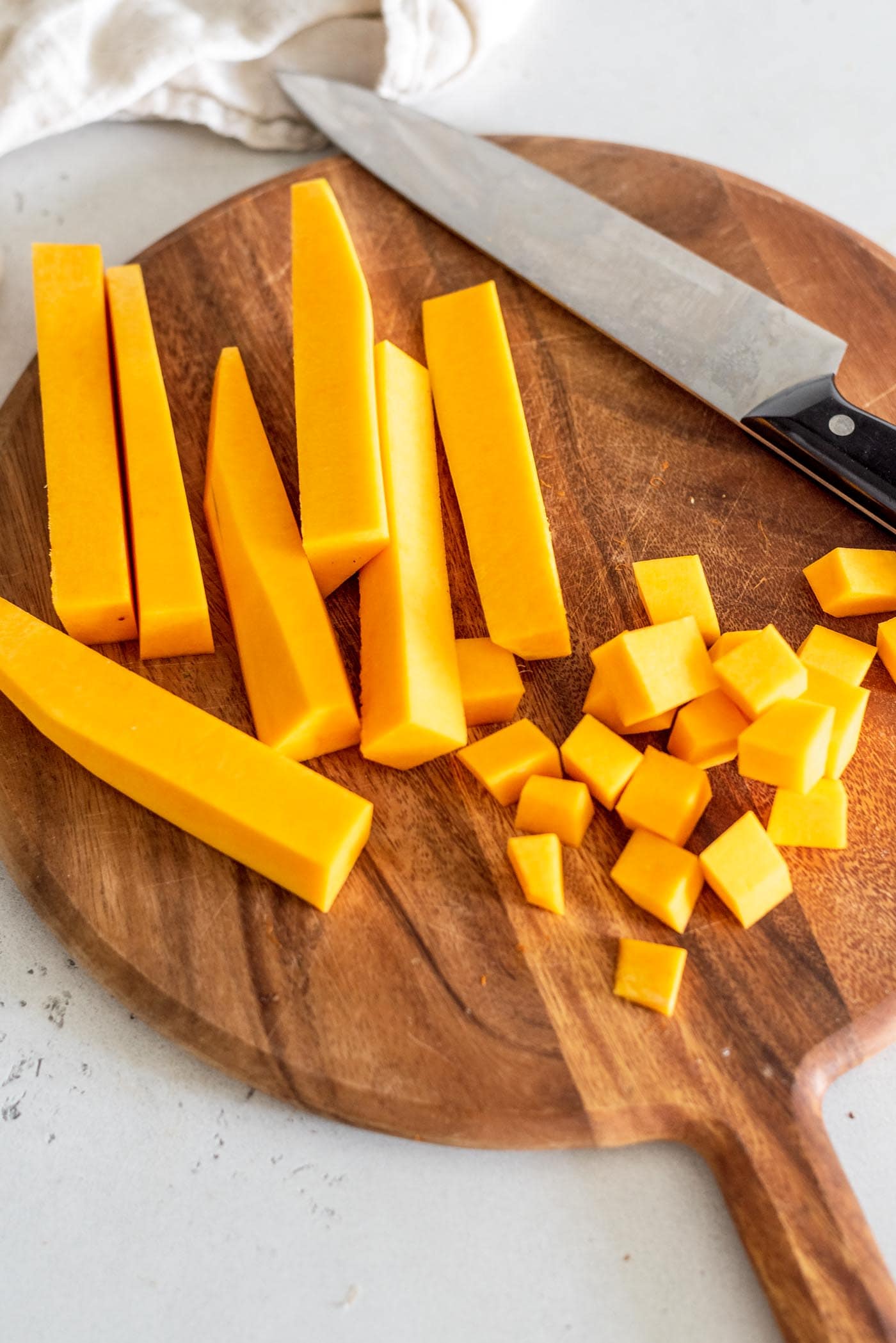 Peeled butternut squash chunks on a cutting board with a knife.