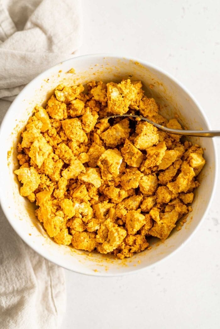 Crumbled firm tofu mixed with turmeric in a white bowl.