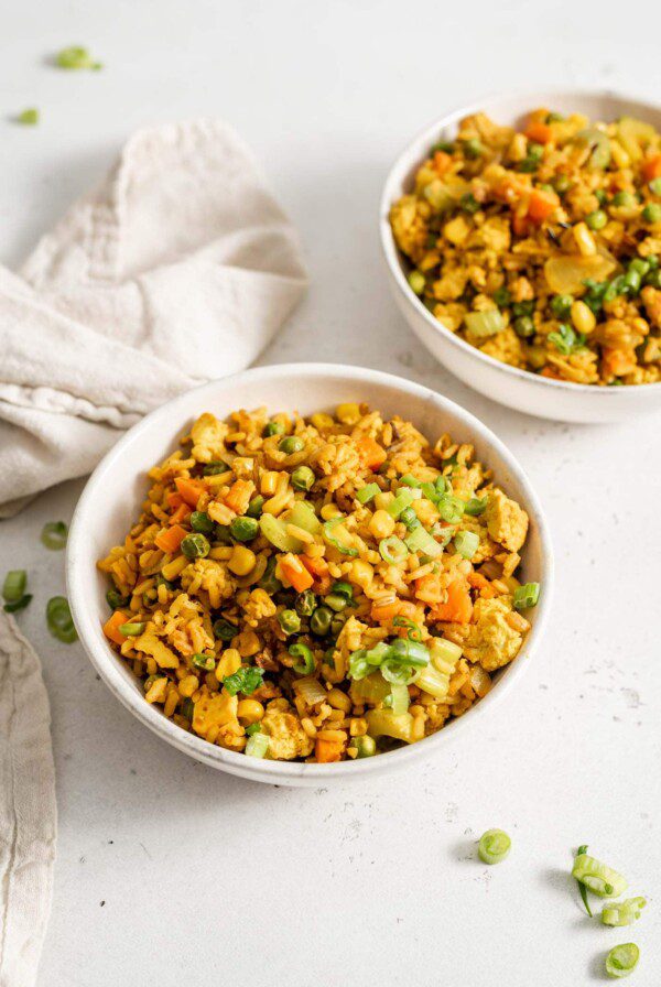 Two bowls of vegan fried brown rice sitting on a white surface.