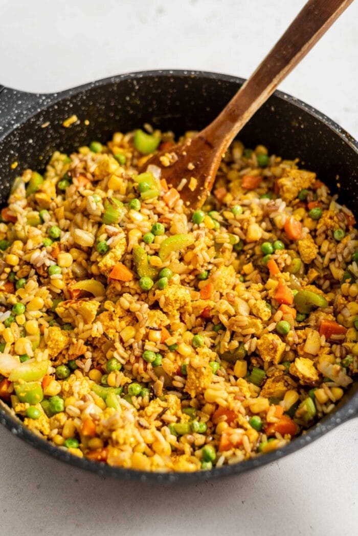 Vegan fried brown rice in a large skillet with a wooden spoon.