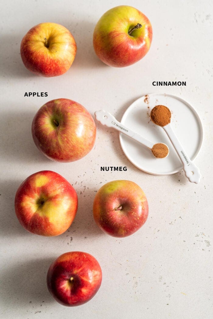 6 apples, 1 tsp of cinnamon and 1/2 tsp of nutmeg on a white surface.