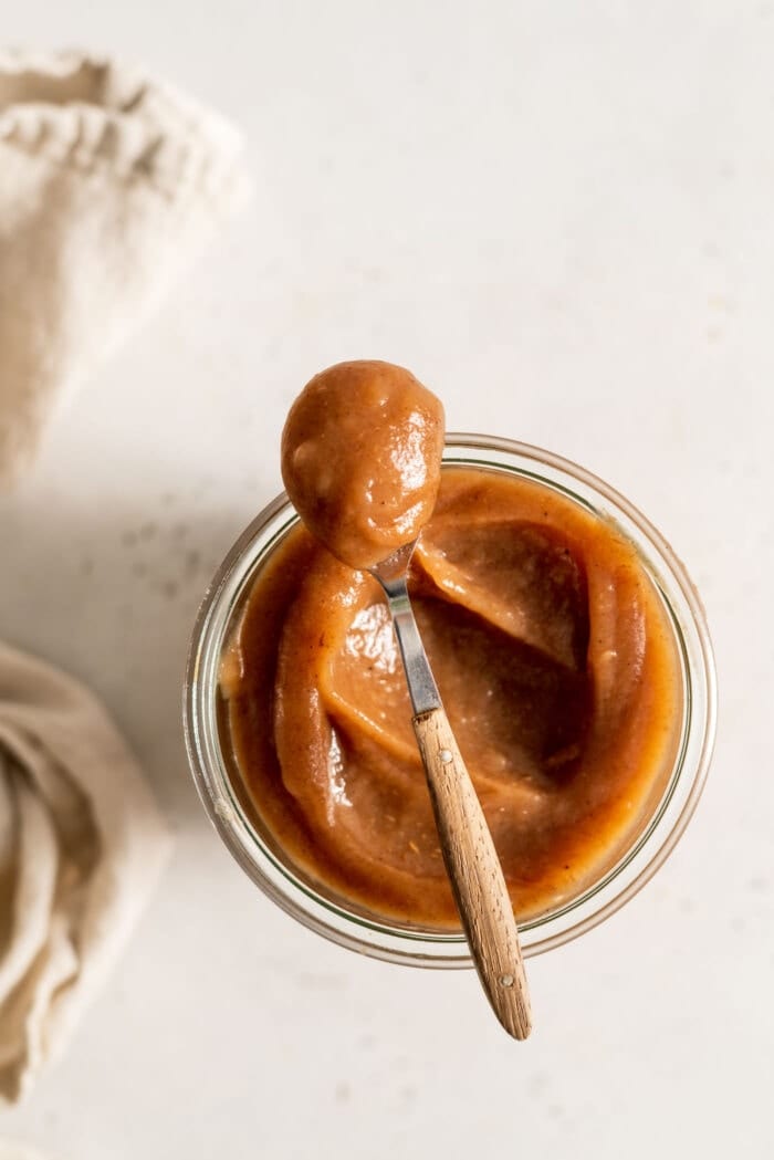 A spoon scooping apple butter out of a glass jar.